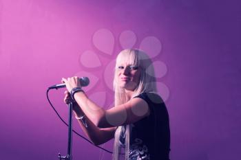 Rock star female sing in stage microphone on violet pink background, side view.