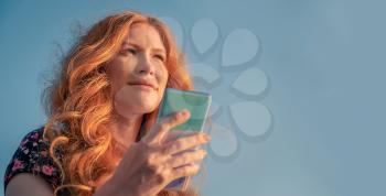 Pretty nice ginger lady in summer dress using smartphone in front of the sky.
