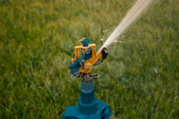Head of tripod sprinkler watering grass.