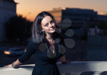 Brunette women posing near balustrade against evening sky