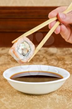 hand holding sushi with chopsticks at table