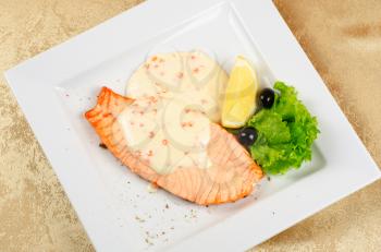 Grilled salmon steak with sauce of cheese and caviar, greens, lemon and olive
