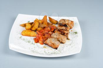 Grilled kebab meat with onion and tomato on a white plate