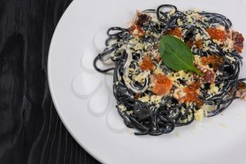 Black pasta with cuttlefish ink, parmesan cheese basil and red caviar. The concept of Italian cuisine.