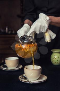 Pouring tea with sea buckthorn honey and herbs in glass teapot