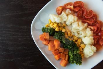 Boiled carrot broccoli corn cauliflower tomato on white plate. Concept. Healthy food. Low-Carb Diet. Vegetarian food.