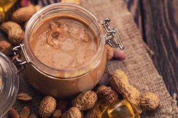 Natural peanut butter with oil in a glass jar and peanuts