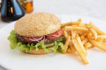 Tasty classical burger with fried potato on white table