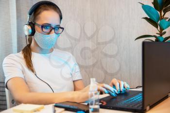 Woman in mask, working from home. Sanitizer anti virus spray on the working table. Coronavirus, quarantine for COVID-19 concept.