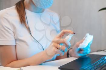 Woman disinfects the surface of the phone by sanitizer spray on the working place.