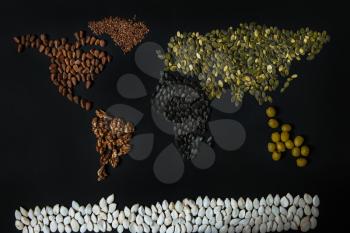 World map from different seed: walnut, olives, flaxseed, pumpkin seed on black background