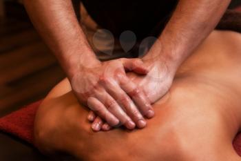 Close-up masseur hands doing back massage to woman in spa center.