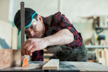 The worker makes measurements of a wooden board with corner ruler.