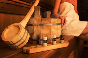 Wooden bath accessories with aromatic oil bottle for bath in the sauna and woman on background
