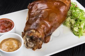 Tasty pork knuckle with sauces and vegetables on a white background