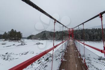 Suspension hanging bridge above winter frozen mountain Katun river, Altai mountains, Siberia, Russia