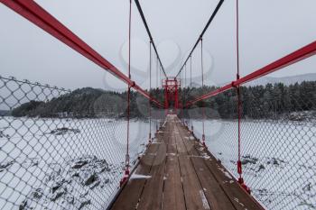 Suspension hanging bridge above winter frozen mountain Katun river, Altai mountains, Siberia, Russia