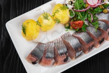 Sliced salted herring with vegetables on white plate