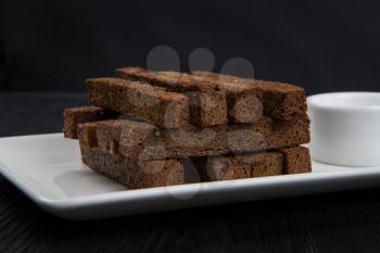 Crackers with garlic from black bread in oil on a wooden black background.