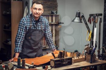 Man working with leather textile r at a workshop. Male portrait. Concept of handmade craft production of leather goods.