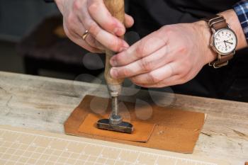 Man makes a stamp on the leather textile at a workshop. Concept of handmade craft production of leather goods.