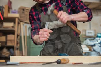 Carpenter working with a chisel and hammer in a wooden workshop. Profession, carpentry and manual woodwork concept.