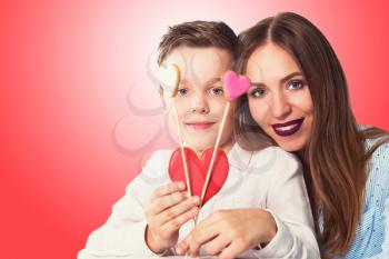 Happy Valentines Day or Mother day. Young boy spend time with his mum and celebrate with gingerbread heart cookies on a stick on a red background