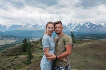 Romantic couple in the mountain, in Altai Mountains. Happy man and woman hug on the background of a mountain glacier, smiling and and look into the camera
