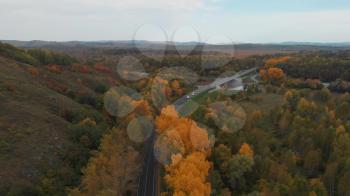 Aerial video of road in beautiful autumn Altai forest. Beautiful landscape with rural road, golden autumn in Altai: trees with red, yellow and orange leaves.