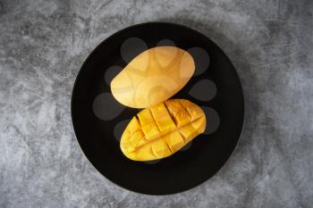 Fresh yellow mango fruit in a black plate on grey stone backgrounds