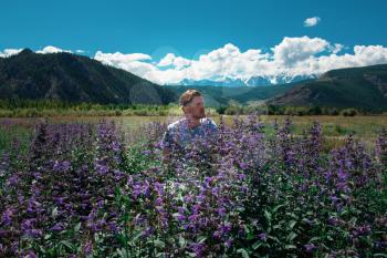 Man in beautiful wild pink and purple flowers field in summer Altai mountains