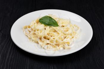 Pasta with sauce and basil in plate on black wooden background