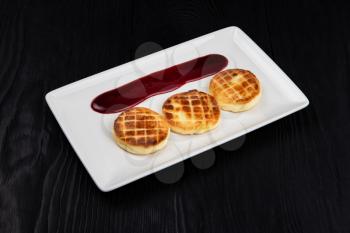 Cottage cheese pancakes on a dark background. Syrniki with berries jam on a white plate, food and drink concept