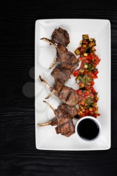 Roasted lamb ribs with vegetables on white palte on black wooden background