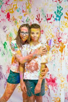 Portrait of a cute happy woman with her son painting and having fun. They are showing their hands face and clothes painted in bright colors