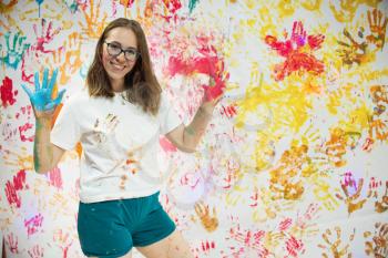 Portrait of a cute happy woman painting and having fun. She is showing her hands face and clothes painted in bright colors