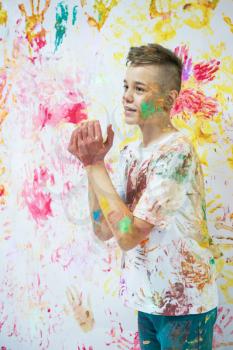 Portrait of a cute happy boy painting and having fun. He is showing his hands face and clothes painted in bright colors