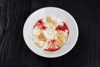 Rice milk porridge with strawberry jam and apple jam in white plate on black wooden background