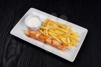 Grilled salmon fish shashlik with fried potatoes and sauce on white plate on black wooden background