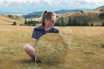 Man standing in in summer Altai mountains in Kurai steppe and holding circle mirror. Creative travel concept