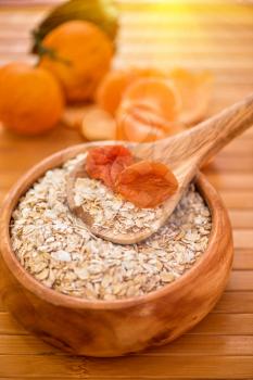 Oat flakes with  dried apricots at wooden plate on fruit background