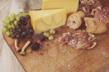 Fresh grapes, cheese bacon berries and salami on wooden table. Toned photo