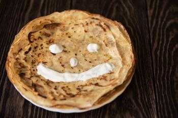 Fried smiling pancakes with sour cream on old wooden table