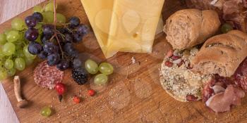 Fresh grapes, cheese bacon berries and salami on wooden table