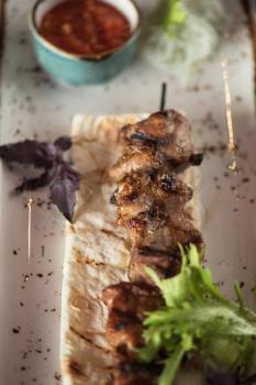 Grilled kebab pork meat with sauce and greens