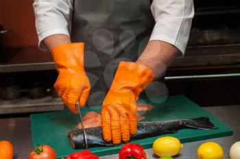 Chef cutting salmon fish on steaks with knife