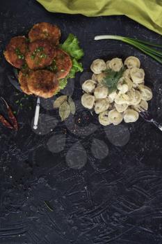 Fried cutlets and russian pelmeni on black background. Food set. Top view.