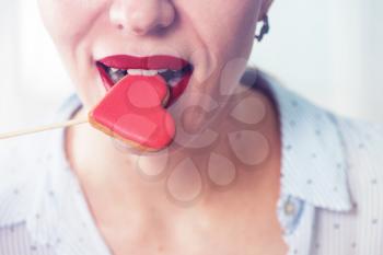 Closeup photo of the woman lips and gingerbread hearts on a stick, concept of love or valentines das