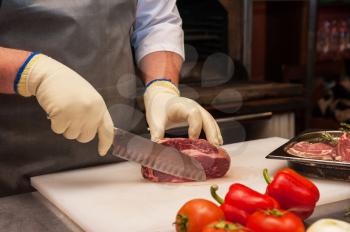 Chef cutting meat on steaks with knife