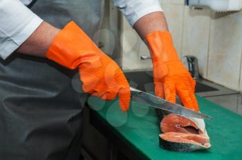 Chef cutting salmon fish on steaks with knife